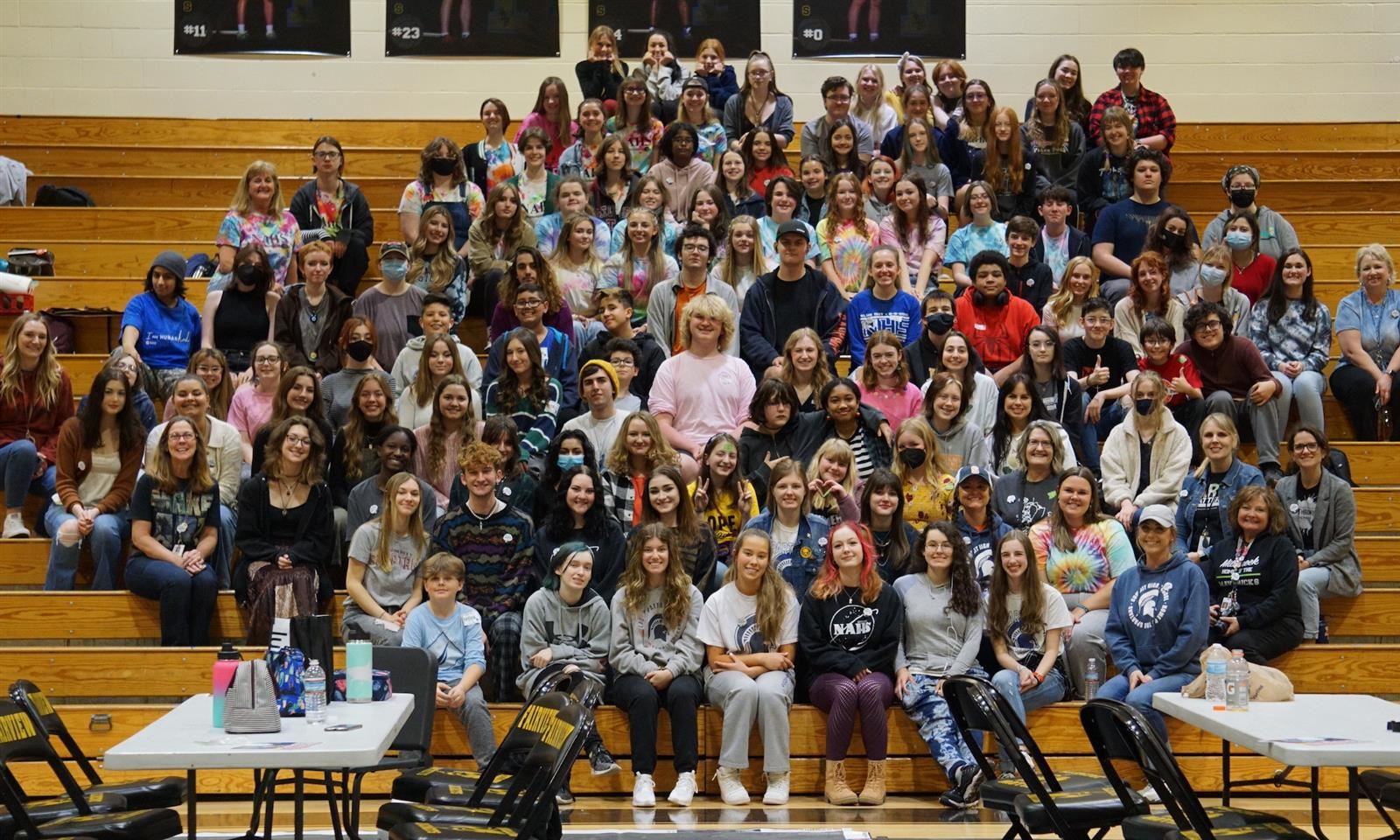 A large group of students sit on bleachers